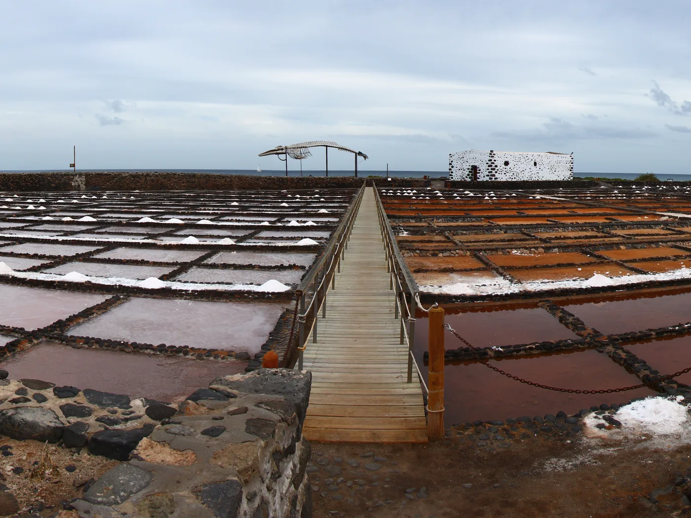 Shallow white salt pans of Salinas del Carmen along the black volcanic coast of Fuerteventura, with the salt museum building behind