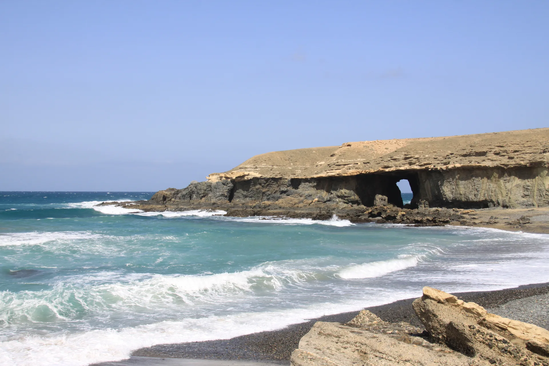 A rocky cove at Playa de Garcey with a large natural rock arch worn into a tan cliff face and turquoise water