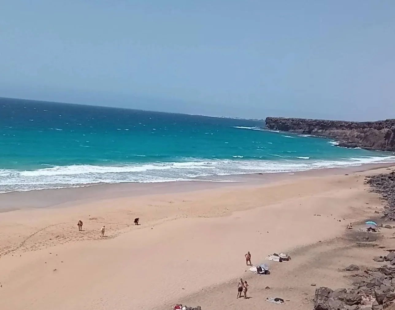 Looking down into the cliff-lined cove at Playa del Águila, with turquoise water, golden sand and a few people on the beach