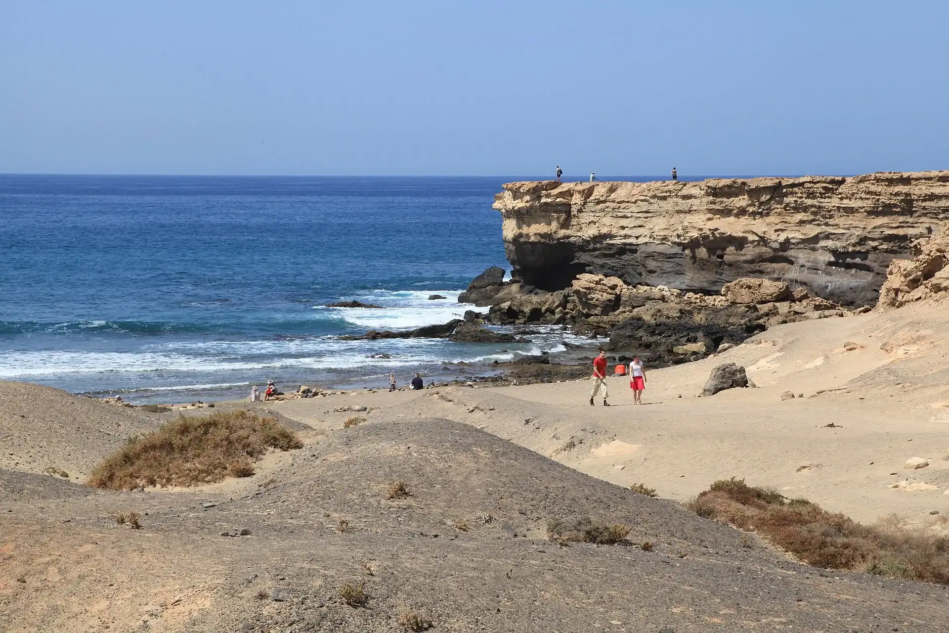Golden-dark sand beach at Playa de la Pared, Fuerteventura, with low cliffs and Atlantic surf breaking offshore