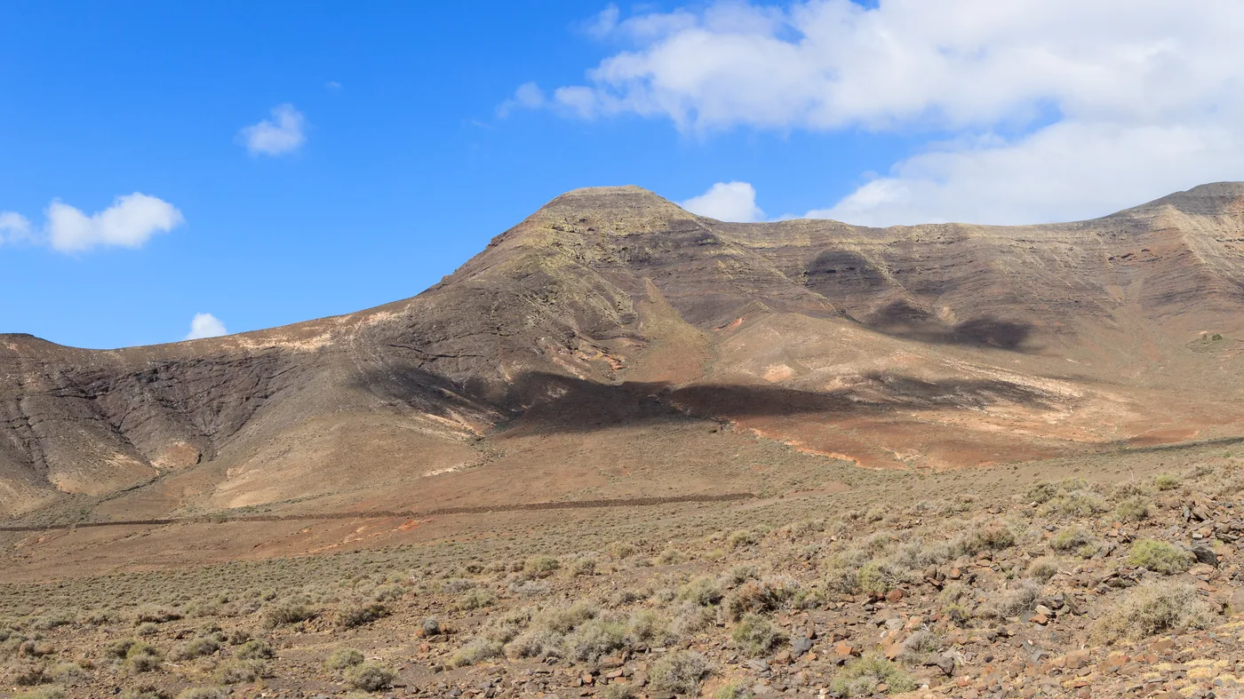 A wide, dry volcanic valley in the Gran Valle, its slopes streaked in shades of brown and red beneath a mountain ridge